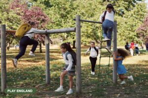 School-age children climbing a wooden play structure in a leafy park