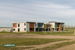 A newly completed suburban school building on a prairie lot, with freshly planted young trees and construction fencing still in place.