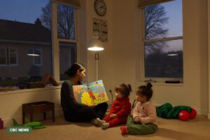 An educator reads a picture book by lamplight to two young children in a warm child care room as dusk shows through the window